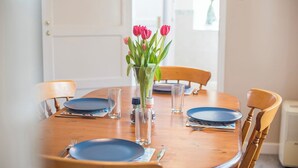 Une table à manger dressée avec des assiettes bleues, des verres transparents et un vase rempli de fleurs roses.