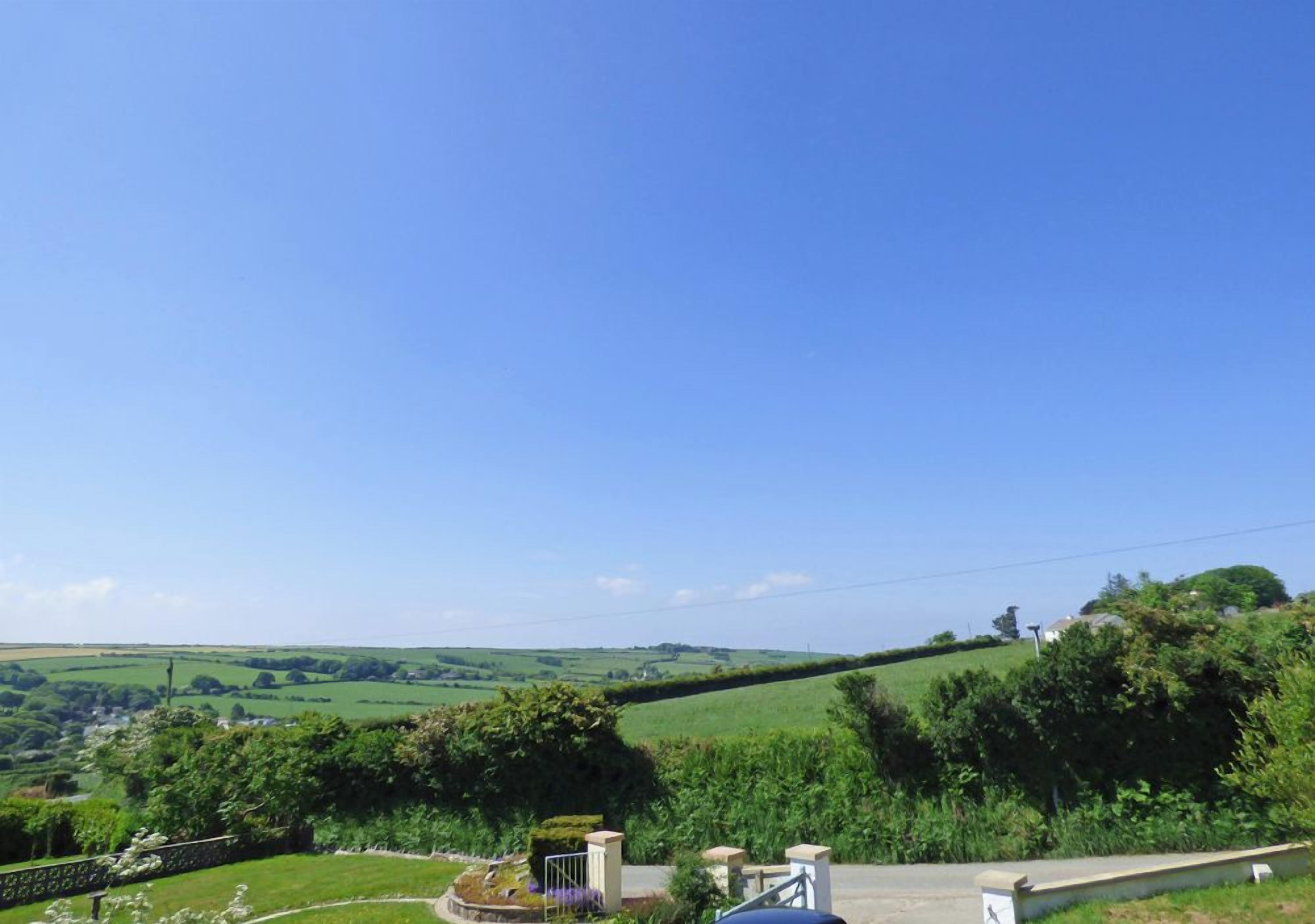 A rural landscape with rolling green hills, a clear blue sky, and a stone wall.