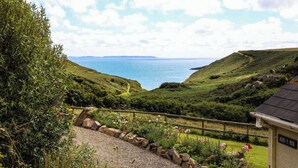 Un paysage côtier avec un sentier de gravier, un mur de pierre et un panneau indiquant « AGOS Y-MOR ».