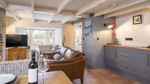 A cozy living room with a brown leather sofa, a wooden dining table with a bottle of wine and glasses, a television, and a patterned rug. - Alma Cottage, Holiday Cottage Solva, Sleeps 3, 2 bedrooms,  bathrooms (Haverfordwest)