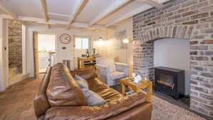 A cozy living room with a stone fireplace, a leather sofa, a patterned armchair, and a dining area with a wooden table and chairs. - Alma Cottage, Holiday Cottage Solva, Sleeps 3, 2 bedrooms,  bathrooms (Haverfordwest)