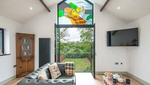 A modern living room with a large window, a black leather sofa, a wooden coffee table, and a television.