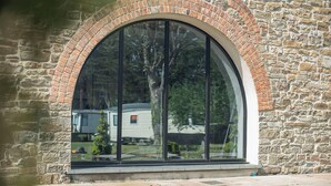 A stone building with a large arched window reflecting a mobile home and trees.