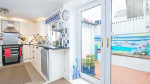 A modern kitchen with white cabinets, a stainless steel oven, a dishwasher, and a window overlooking a colorful outdoor mural. - Anvil House, Holiday Home Tenby, Sleeps 8, 4 bedrooms,  bathrooms (Tenby)