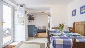 A dining area with a checkered tablecloth, a blue sofa, and a dining table set with plates, bowls, and a vase of flowers. - Anvil House, Holiday Home Tenby, Sleeps 8, 4 bedrooms,  bathrooms (Tenby)
