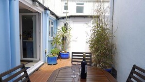 A wooden table with two chairs, a bottle of wine, and two glasses on a balcony with potted plants and a door leading to a room. - Anvil House, Holiday Home Tenby, Sleeps 8, 4 bedrooms,  bathrooms (Tenby)