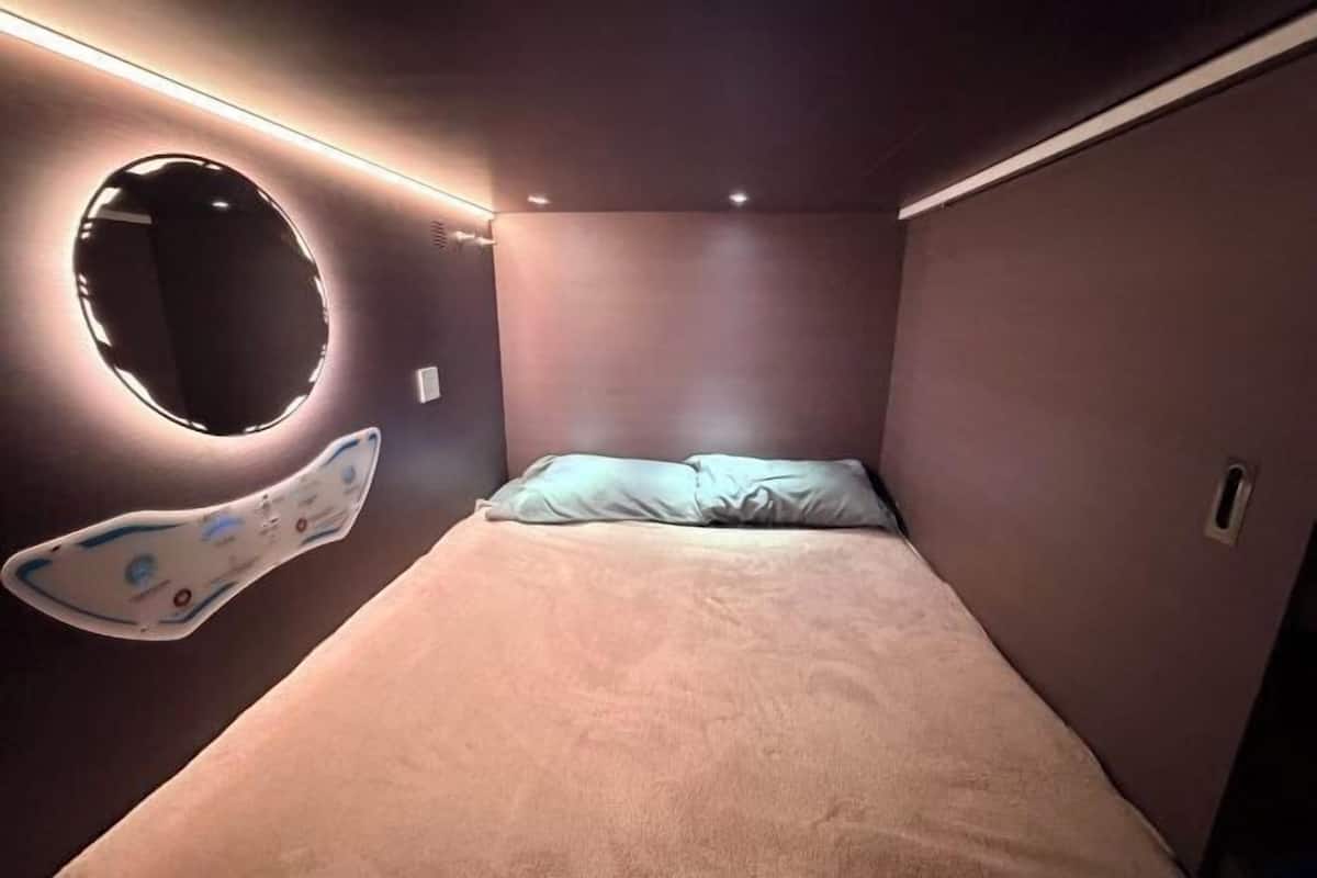 Een kleine, gezellige kamer met een enkel bed, een ronde spiegel en een wandlamp.
