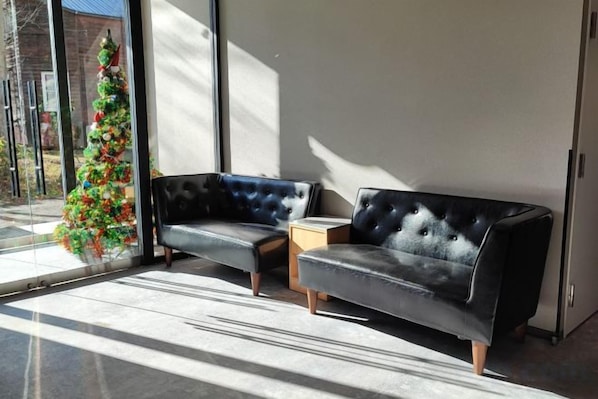 A modern room with a black leather sofa, a small wooden side table, and a Christmas tree. - Q Fox Black Diamond Hotel (Kutchan)