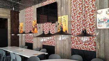 A restaurant interior with a long table, multiple chairs, hanging pendant lights, and a patterned wall.