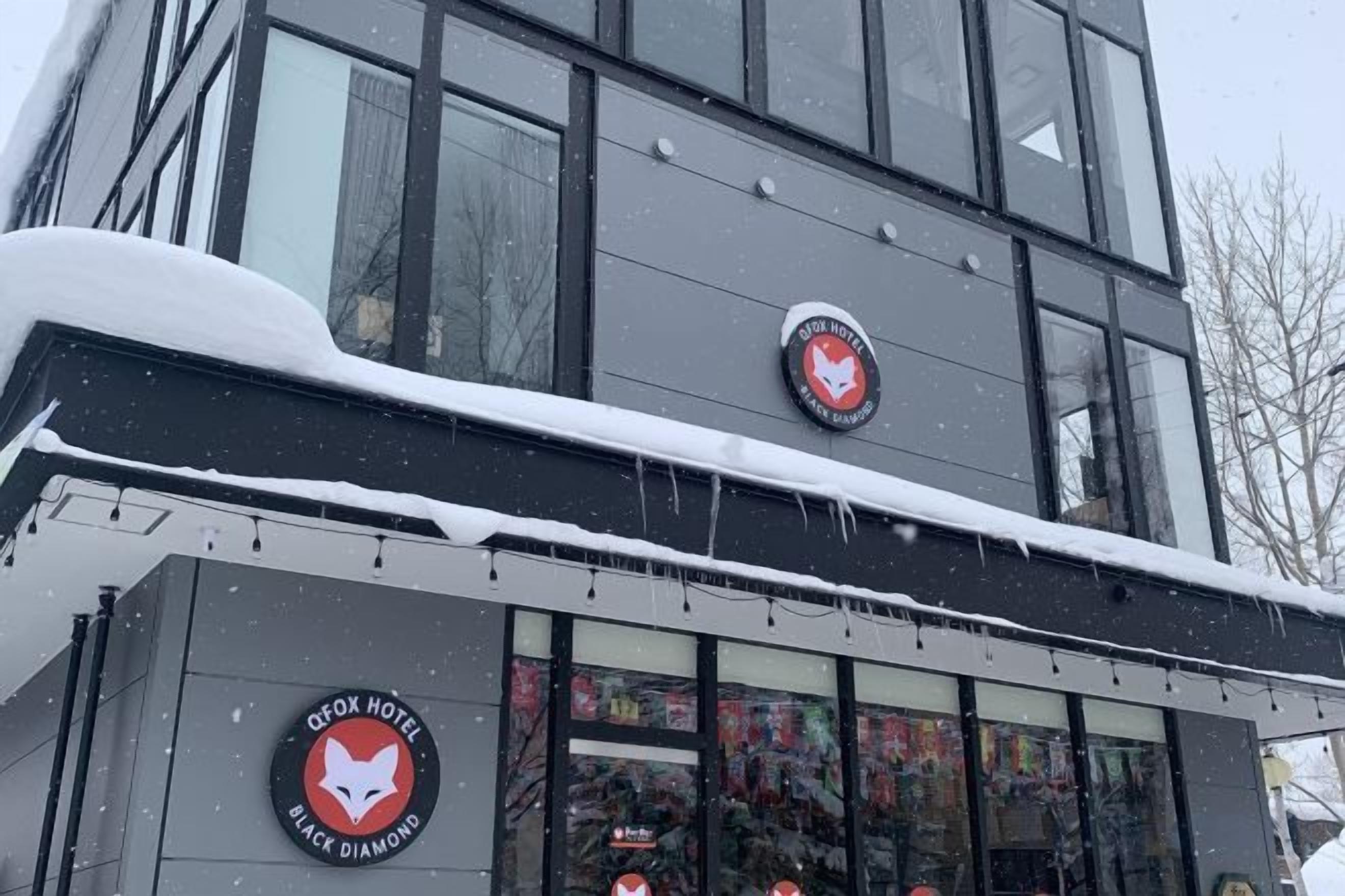 Un hotel con una fachada moderna, grandes ventanales y acumulación de nieve en el tejado.