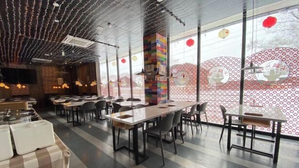 Un restaurante moderno con mesas comunes largas, sillas negras y una pared con diseños circulares.