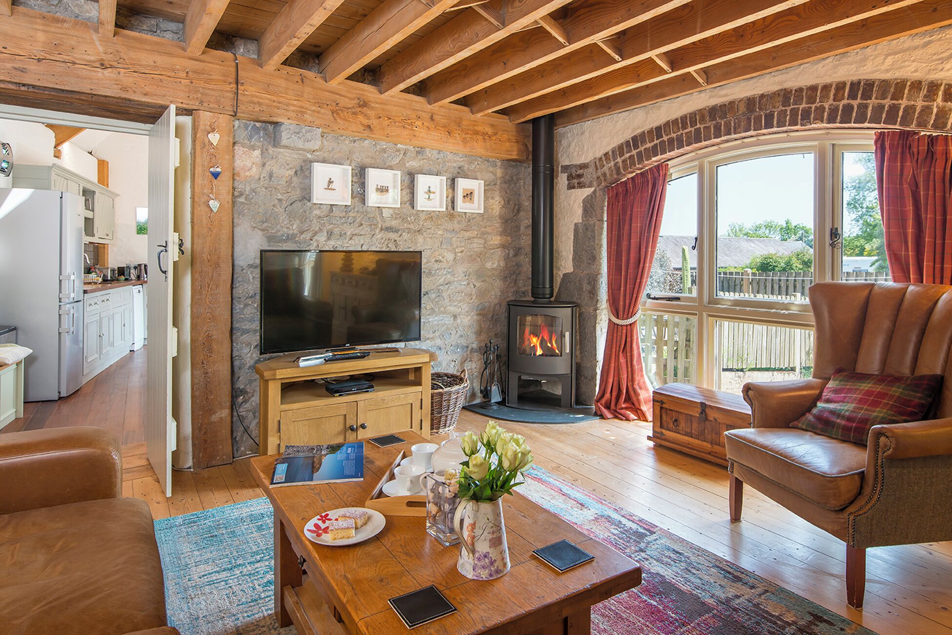 A cozy living room with a stone wall, wooden beams, a fireplace, a television, and a leather armchair.