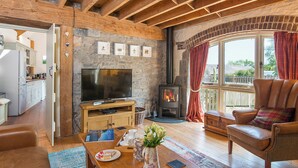 A cozy living room with a stone wall, wooden beams, a fireplace, a television, and a leather armchair. - Arch Barn, Holiday Cottage St Twynnells, Nr Bosherston | Stackpole, Sleeps 6, 3 bedrooms,  bathrooms (PEMBROKE)