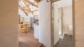 A modern kitchen with wooden flooring, a dining area with a table and chairs, and a glass-enclosed shower area. - Arch Barn, Holiday Cottage St Twynnells, Nr Bosherston | Stackpole, Sleeps 6, 3 bedrooms,  bathrooms (PEMBROKE)