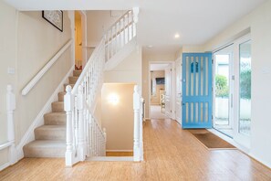 A staircase with white balusters leading to a landing, a blue door with glass panels, and a view of a garden through a glass door. - Atlantic Sunset, Holiday Home Little Haven, Sleeps 12, 6 bedrooms,  bathrooms (Little Haven)