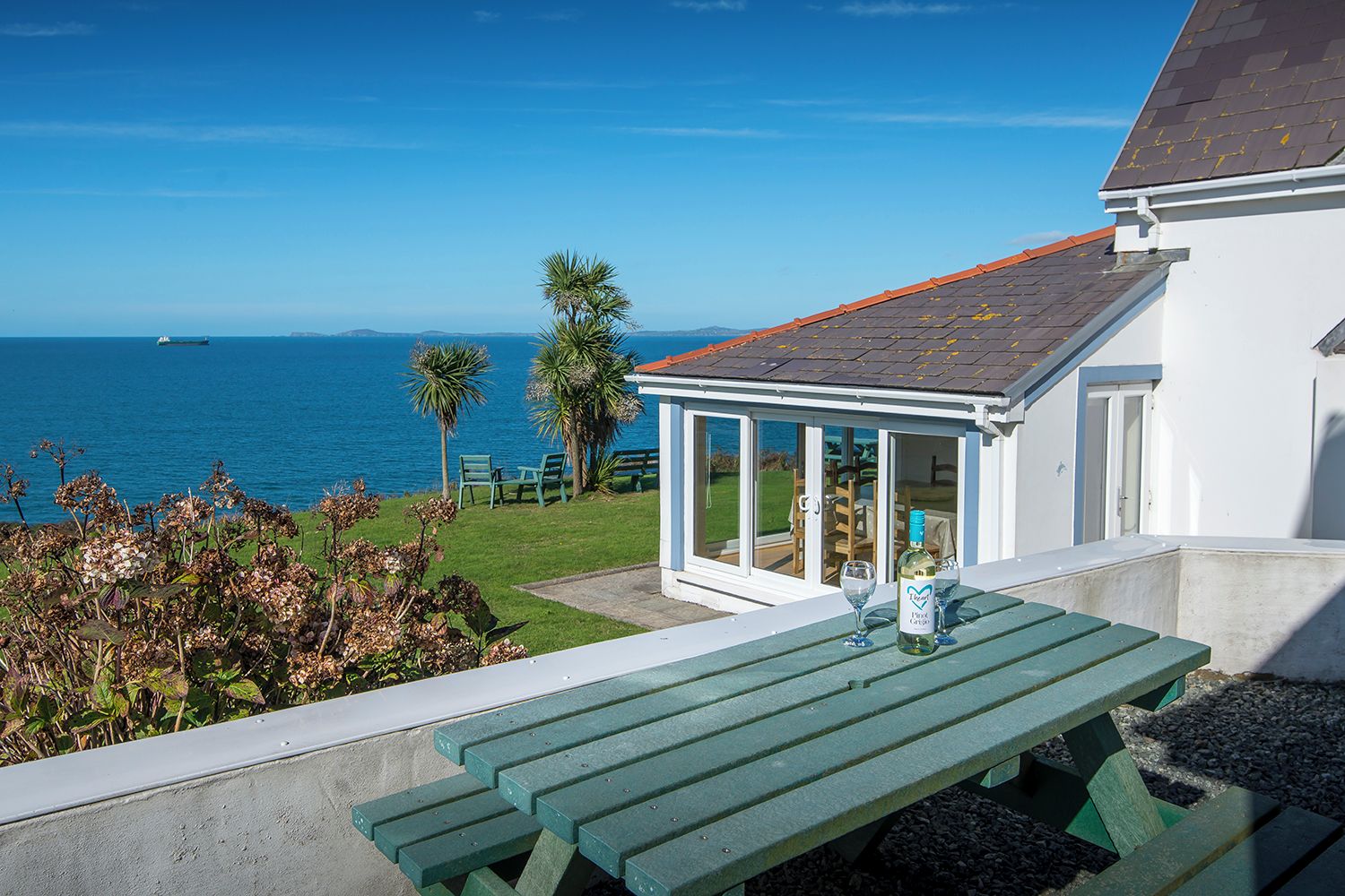 A seaside property with a patio table, chairs, and a glass-enclosed veranda overlooking the ocean.
