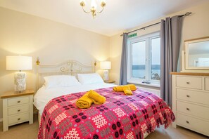 A hotel room with a bed, two bedside tables, a nightstand, a dresser, a mirror, a window with curtains, and a chandelier. - Atlantic Sunset, Holiday Home Little Haven, Sleeps 12, 6 bedrooms,  bathrooms (Little Haven)