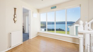 Une pièce spacieuse dotée d’une grande fenêtre donnant sur un lac et des collines, d’un radiateur blanc et d’un plancher en bois.