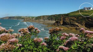Un paysage côtier avec des falaises, une plage et une maison située sur une colline.