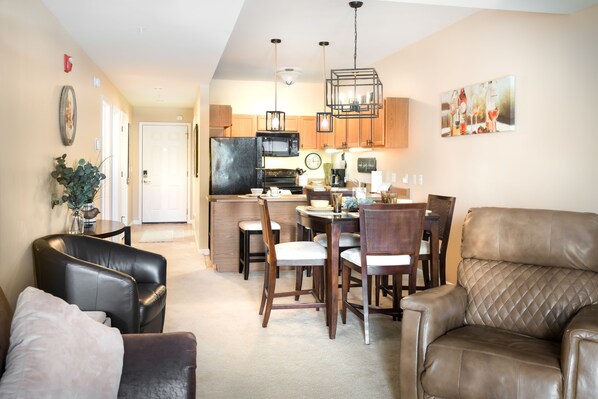 A modern kitchen with wooden cabinets, a black refrigerator, and a dining area with a table and chairs. - River of Peace Condominium! River Side Condo In The Heart of Pigeon Forge! (Sevierville)