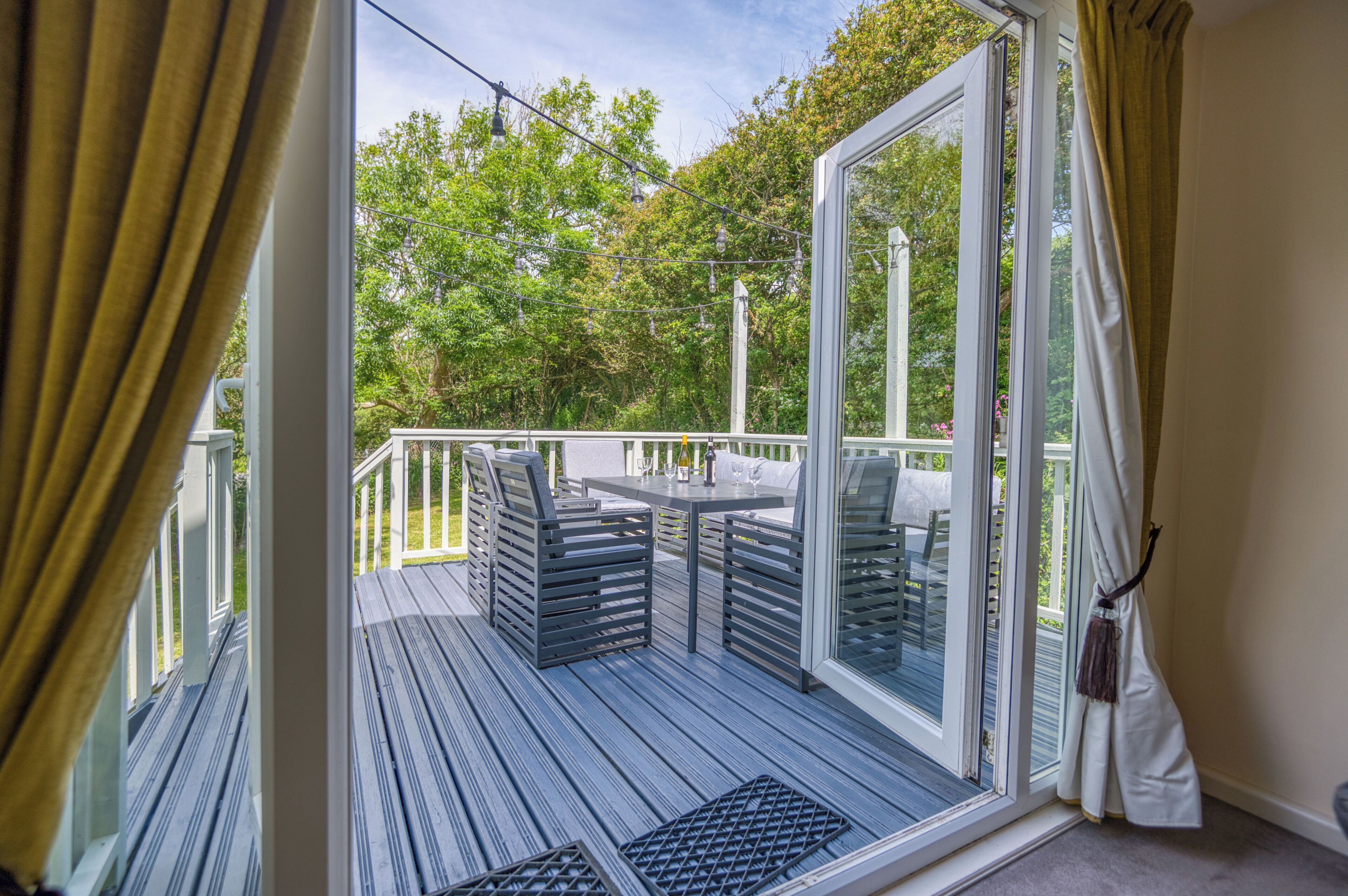 En terrasse med udendørs møbler, en glasdør der fører til en have, og en hvid gardin.