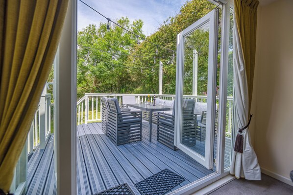 A deck with outdoor furniture, a glass door leading to a garden, and a white curtain. - Avalon, Holiday Home Nolton Haven, Sleeps 6, 3 bedrooms,  bathrooms (Nr Haverfordwest)
