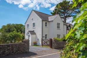 A two-story house with a stone wall entrance, a gated driveway, and a clear sky. - Awel y Mor, Holiday home  Stackpole, Sleeps 6, 3 bedrooms,  bathrooms (Stackpole)