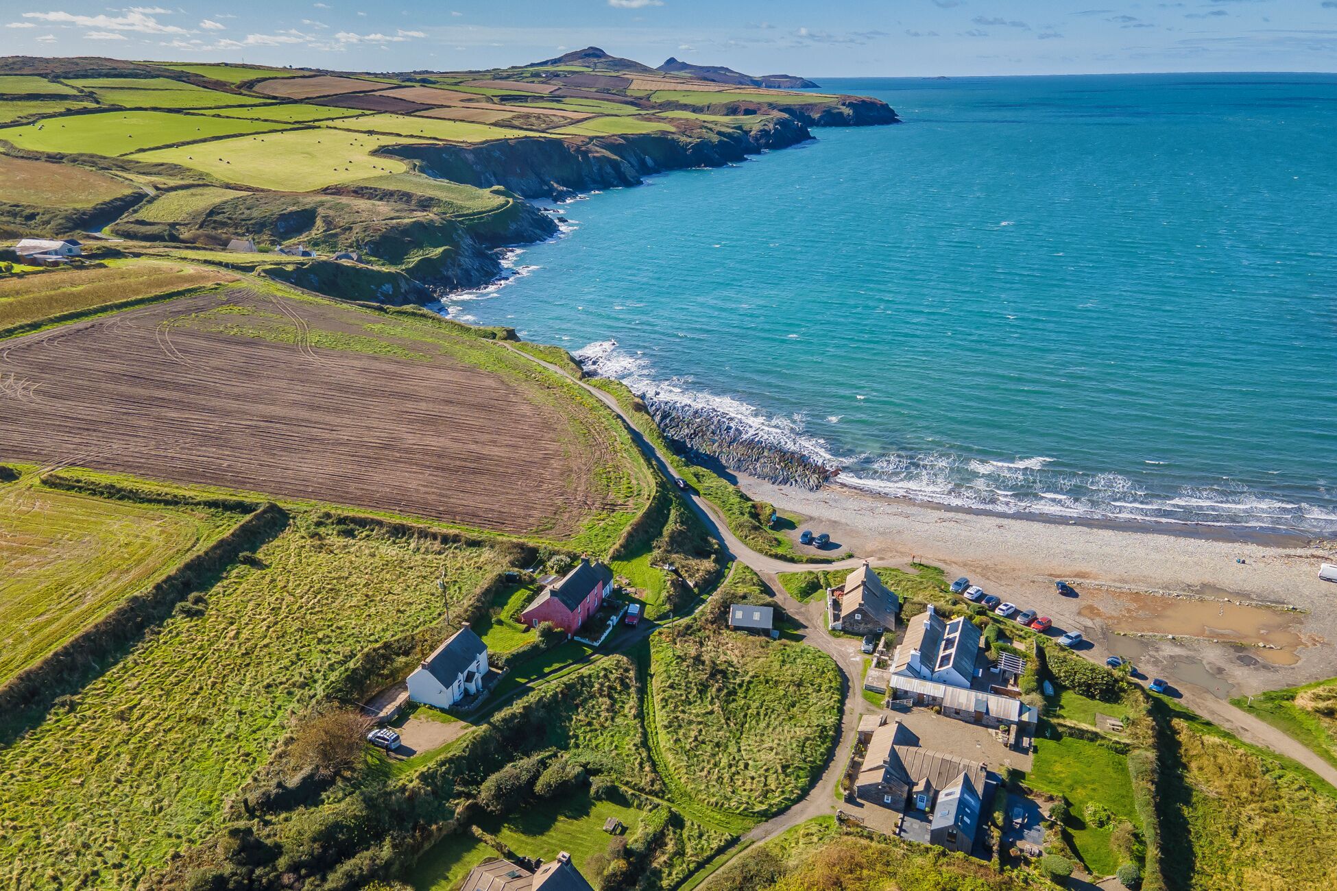Une vue aérienne d’une zone côtière avec des champs, une plage et des bâtiments.
