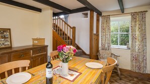 Un coin repas avec une table en bois, des chaises, une bouteille de vin et un vase de fleurs.