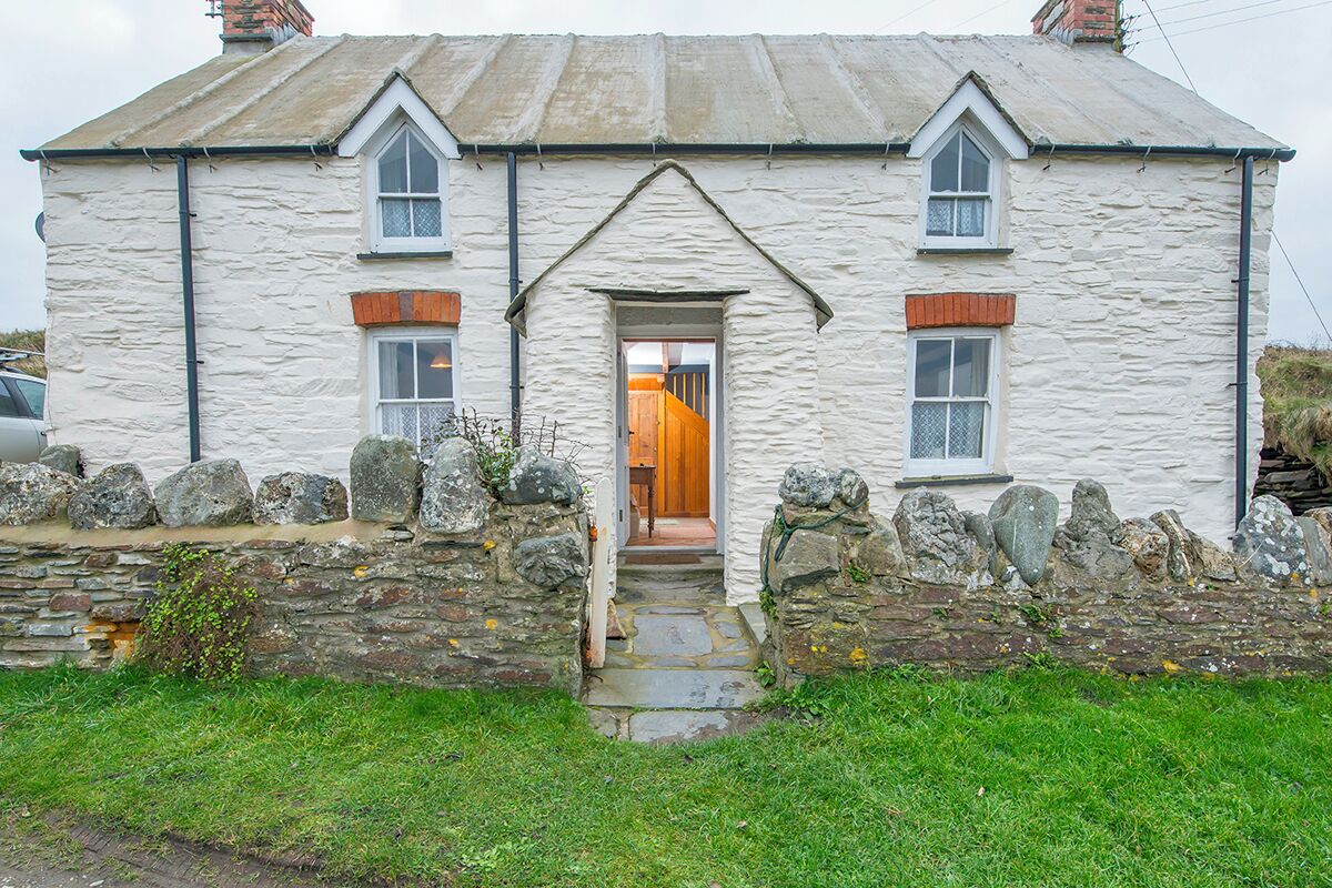 A stone house with a central doorway, two windows on either side, and a small porch area.