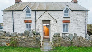 Une maison en pierre avec une porte d’entrée centrale, deux fenêtres de chaque côté et un petit porche.