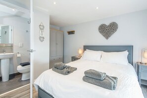 A hotel room with a bed, a nightstand, a bedside lamp, a wall-mounted heart decoration, a wardrobe, and a bathroom with a sink and toilet. - Black Hall Cottage, Holiday Cottage Amroth, Sleeps 6, 3 bedrooms,  bathrooms (Amroth)