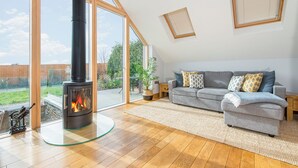 A spacious living room with a large fireplace, a grey sofa, and a view of a garden through large glass doors. - Blackberry Cottage, Holiday Cottage Solva, Sleeps 4, 2 bedrooms,  bathrooms (Haverfordwest)