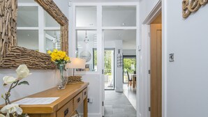 A hallway with a wooden desk, a mirror, and a vase with yellow flowers. There is a door leading to another room. - Brierbank, Holiday Property Tenby, Sleeps 10, 5 bedrooms,  bathrooms (Tenby)