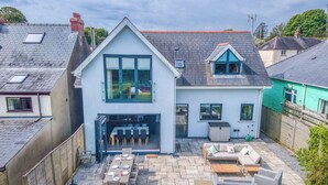 A two-story house with a patio area featuring a table and chairs, a sofa, and a wooden bench. - Brierbank, Holiday Property Tenby, Sleeps 10, 5 bedrooms,  bathrooms (Tenby)