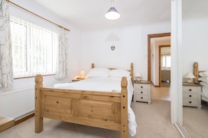 Een slaapkamer met een houten bed, nachtkastjes met lampen, een radiator en een raam met gordijnen.