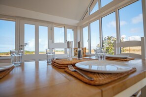 A dining table set with plates, glasses, and cutlery, with a view of the outdoors through large windows.