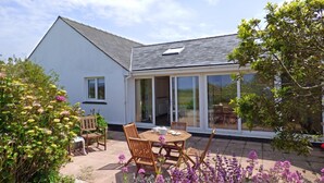 Ein Haus mit einer Terrasse, ausgestattet mit Tisch und Stühlen, umgeben von blühenden Pflanzen.