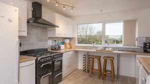 A modern kitchen with a Bosch gas stove, double ovens, a large window with a view, and wooden stools at the island. - Bryngarw, Holiday Home Trefin, Sleeps 12, 6 bedrooms,  bathrooms (Haverfordwest)