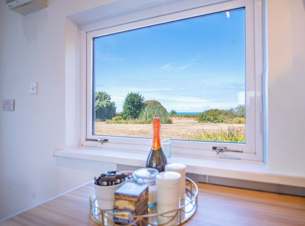 A room with a window overlooking a field, a bottle, and a tray with food items.