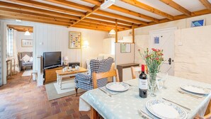 A cozy room with a wooden ceiling, a television, a dining table set with plates and cutlery, and a chair with a plaid pattern. - Bwthyn Bach, Holiday Cottage Trefin, Sleeps 2, 1 bedrooms,  bathrooms (Haverfordwest)