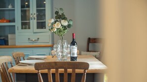 A dining table with a bottle of wine, glasses, and a vase of flowers. - Bwthyn Clyd, Holiday Cottage Keeston, Near Newgale, Sleeps 6, 3 bedrooms,  bathrooms (Haverfordwest)