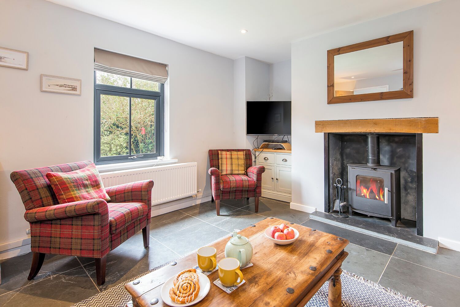 A cozy living room with two plaid armchairs, a wooden coffee table with snacks, a fireplace, and a TV.