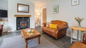 A cozy living room with a fireplace, leather sofa, wooden coffee table, and a small side table with a vase. - Bwthyn Clyd, Holiday Cottage Keeston, Near Newgale, Sleeps 6, 3 bedrooms,  bathrooms (Haverfordwest)