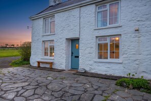 A white house with a blue door, stone steps, and a bench.
