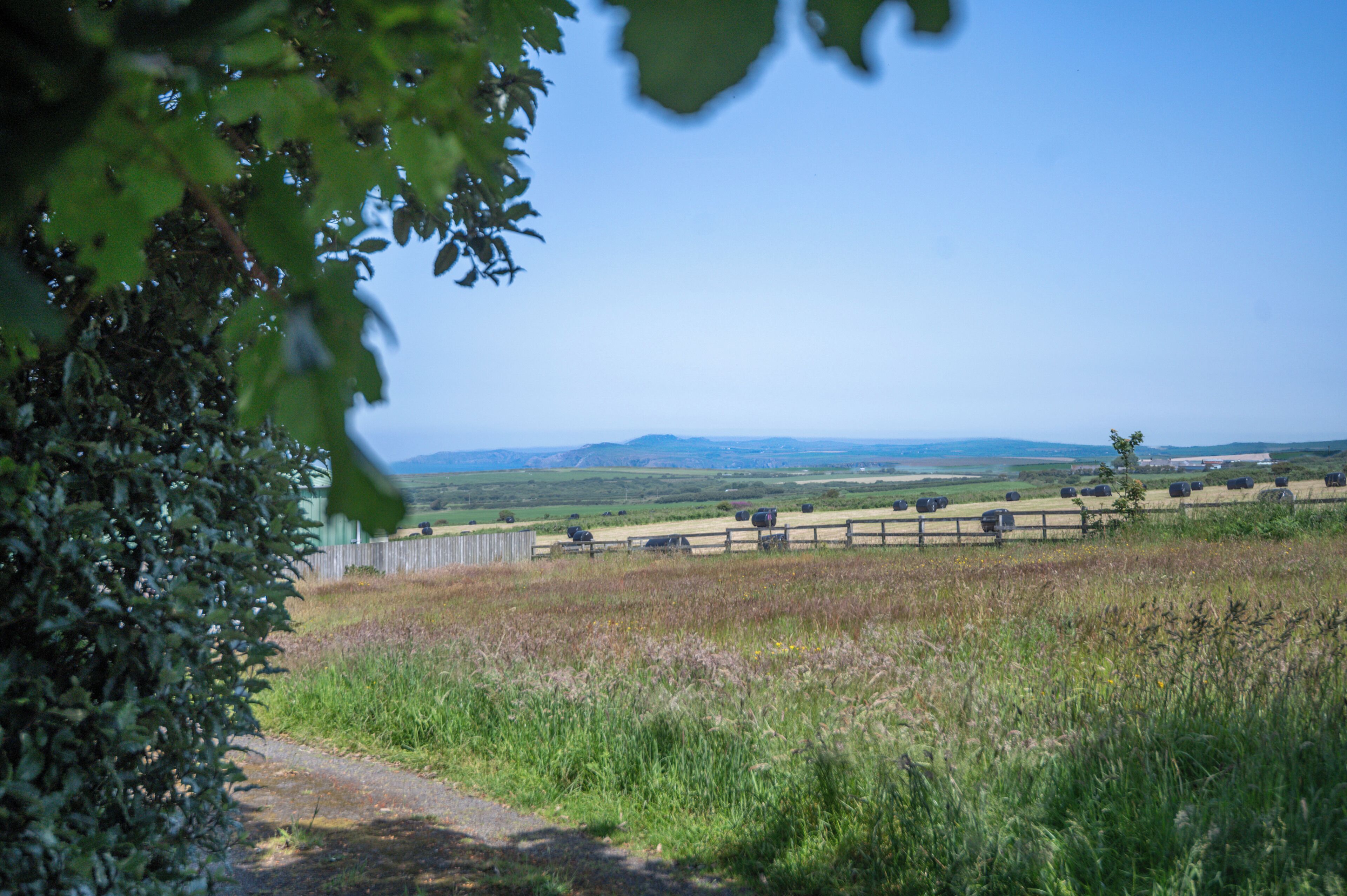A rural landscape with a clear sky, a fenced field, and distant hills.