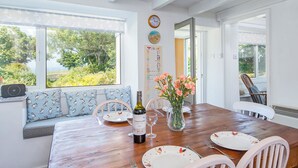 A dining area with a wooden table set for two, a vase of flowers, and a bottle of wine. - 2 Caerau Isaf, Holiday Home Aberfelin Bay, Sleeps 4, 4 bedrooms,  bathrooms (Haverfordwest)