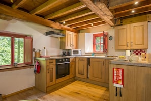 A kitchen with wooden cabinets, a stove, a microwave, and a window with a red curtain.