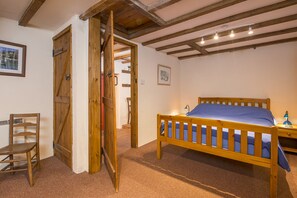 Een slaapkamer met een houten bed, een stoel en een deur naar een andere kamer.