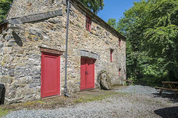 A stone building with two red doors and a wooden picnic table in front.